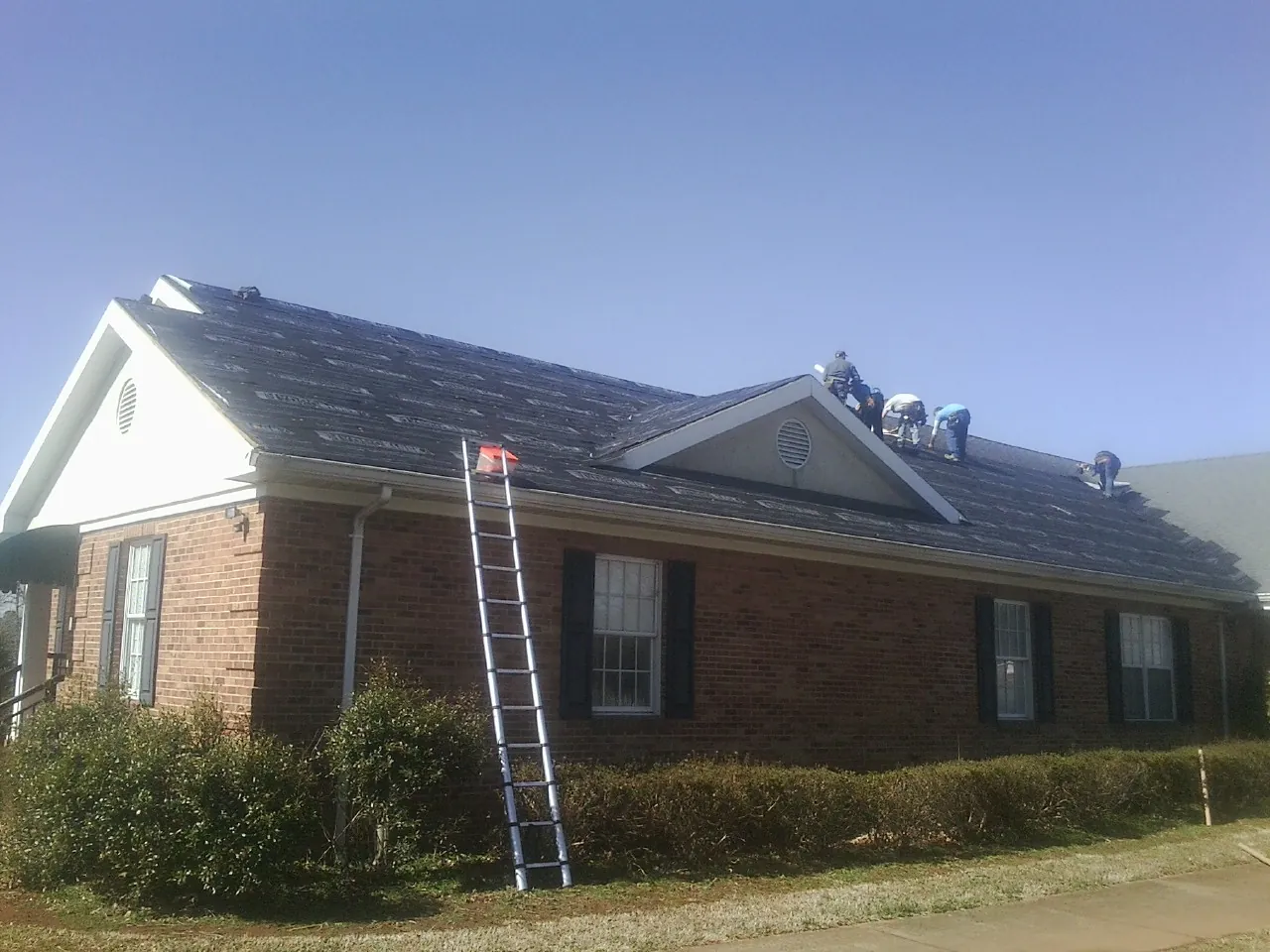 Crew tearing shingles off a brick ranch roof with a ladder set — Emergency Roof Repair work by our crew in Westmont