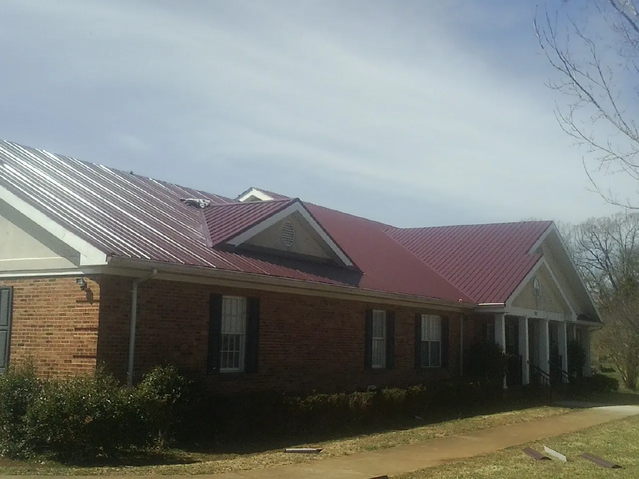 Red metal roof with gabled entries on a long brick building, from a Hail Damage Roof Repair job in Westmont