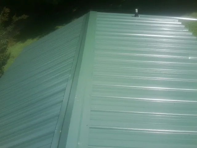 New green metal panels meeting at the ridge of a roof — Flat Roof Repair work by our crew in Westmont