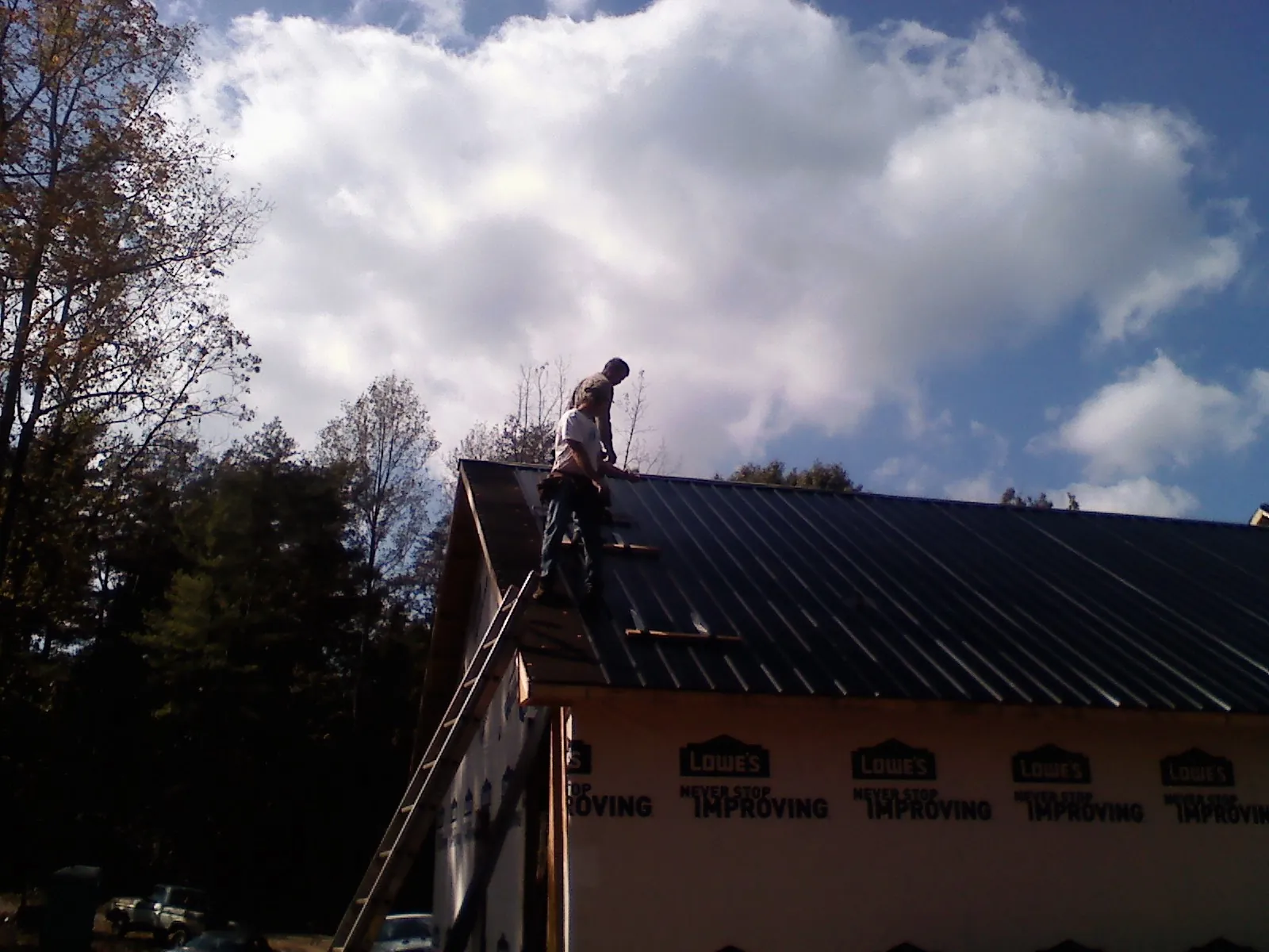Roofer fastening dark metal panels high against a cloudy sky, from a Roof Inspection job in Westmont