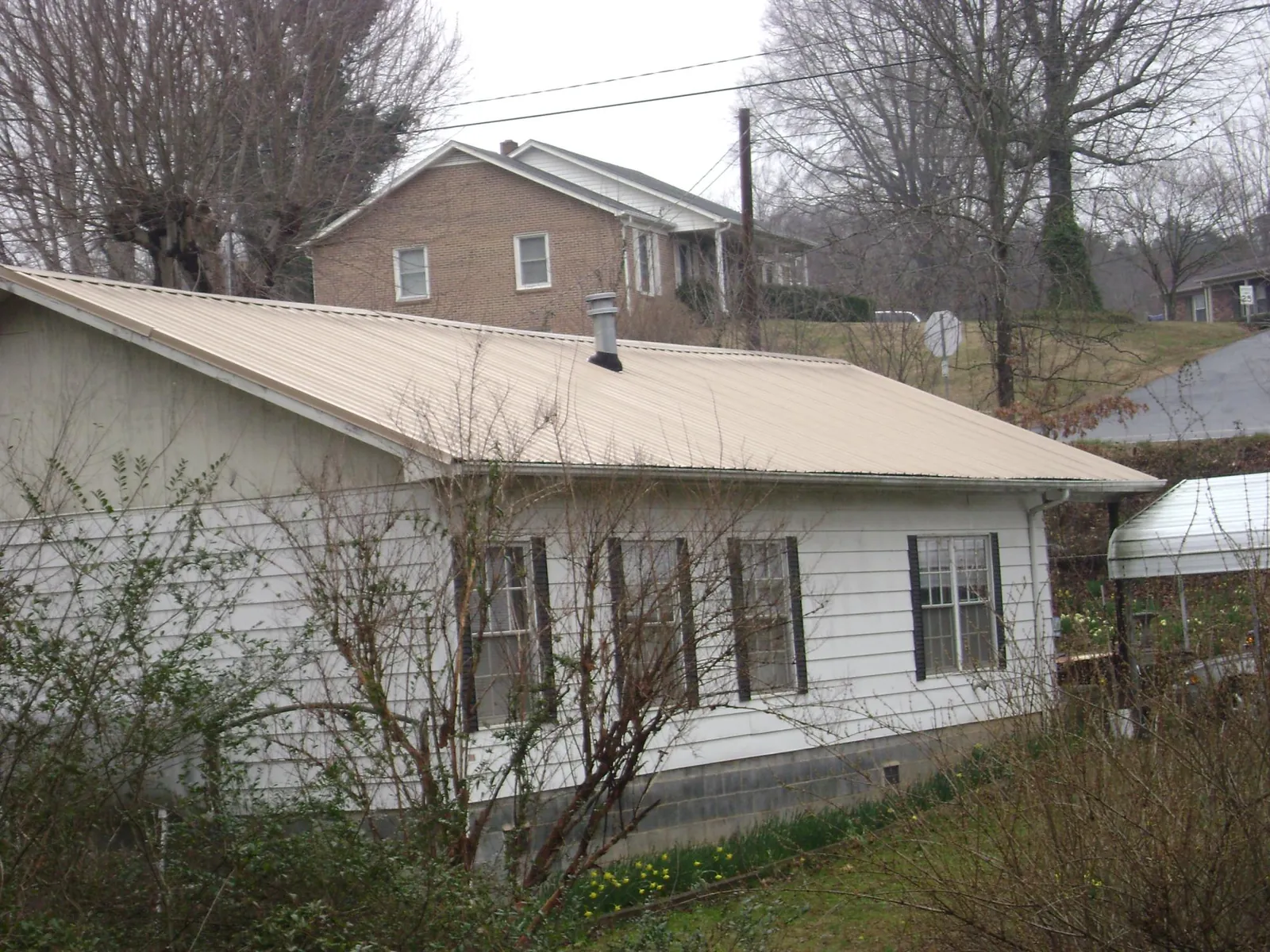 Tan metal roof on a white sided house set into a hillside — Commercial Roofing by Roofing Brothers in Westmont